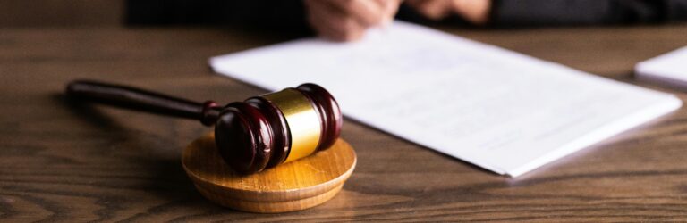 Judge's gavel on a desk with a person signing documents in the background, symbolizing the legal process for protection orders